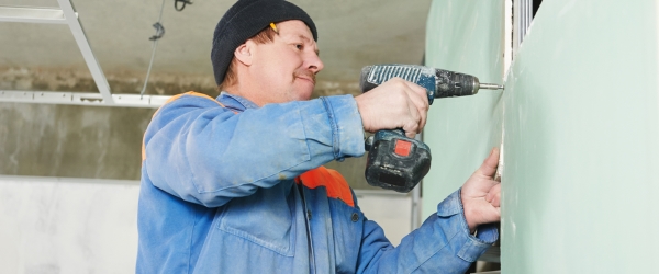 carpenter with gypsum plasterboard and screwdriver